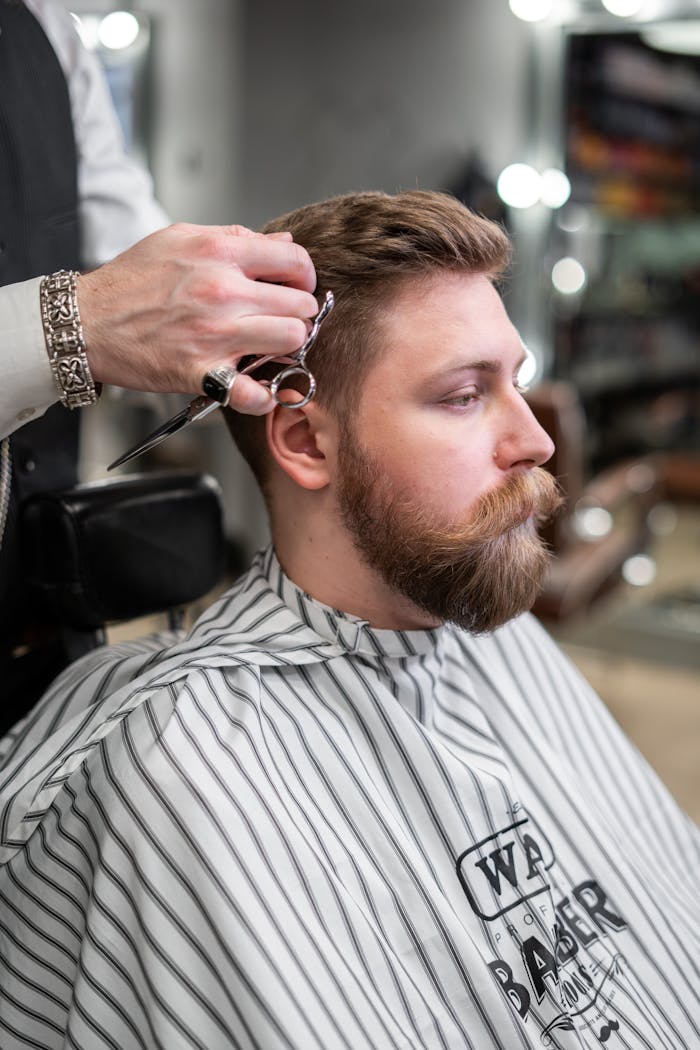 services-02 A barber trims a bearded mans hair in a classic barbershop setting.