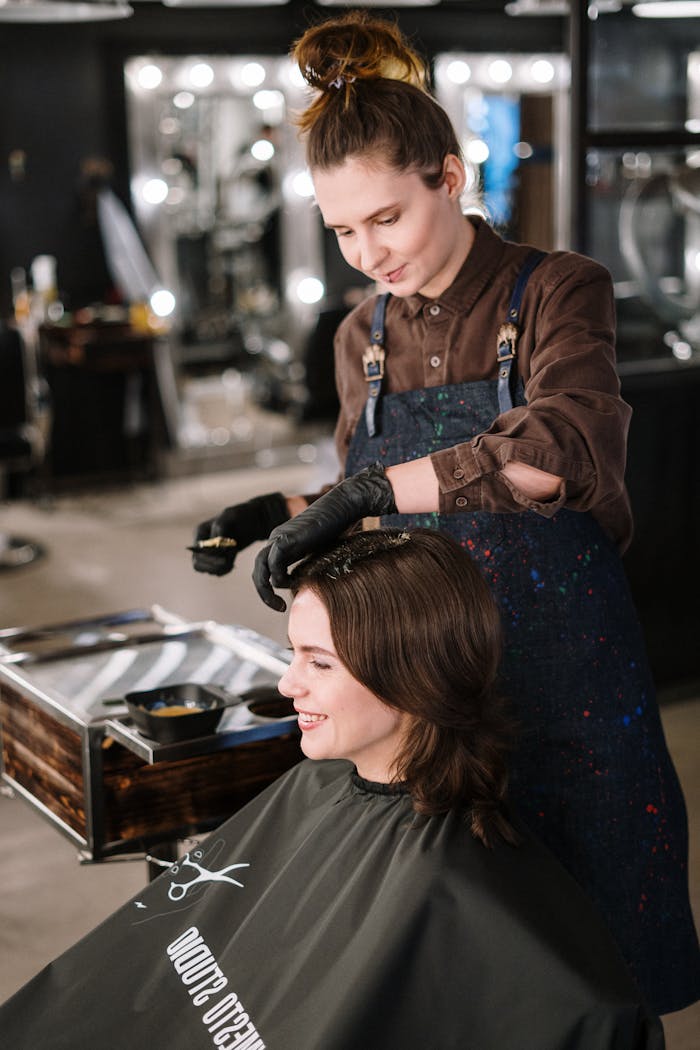 services-03 Hairdresser applying color to womans hair in a modern salon, capturing a lively professional atmosphere.
